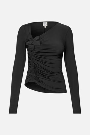 Front view of a black long-sleeve top with an asymmetrical neckline, gathered side ruching and a fabric flower detail at the shoulder.
