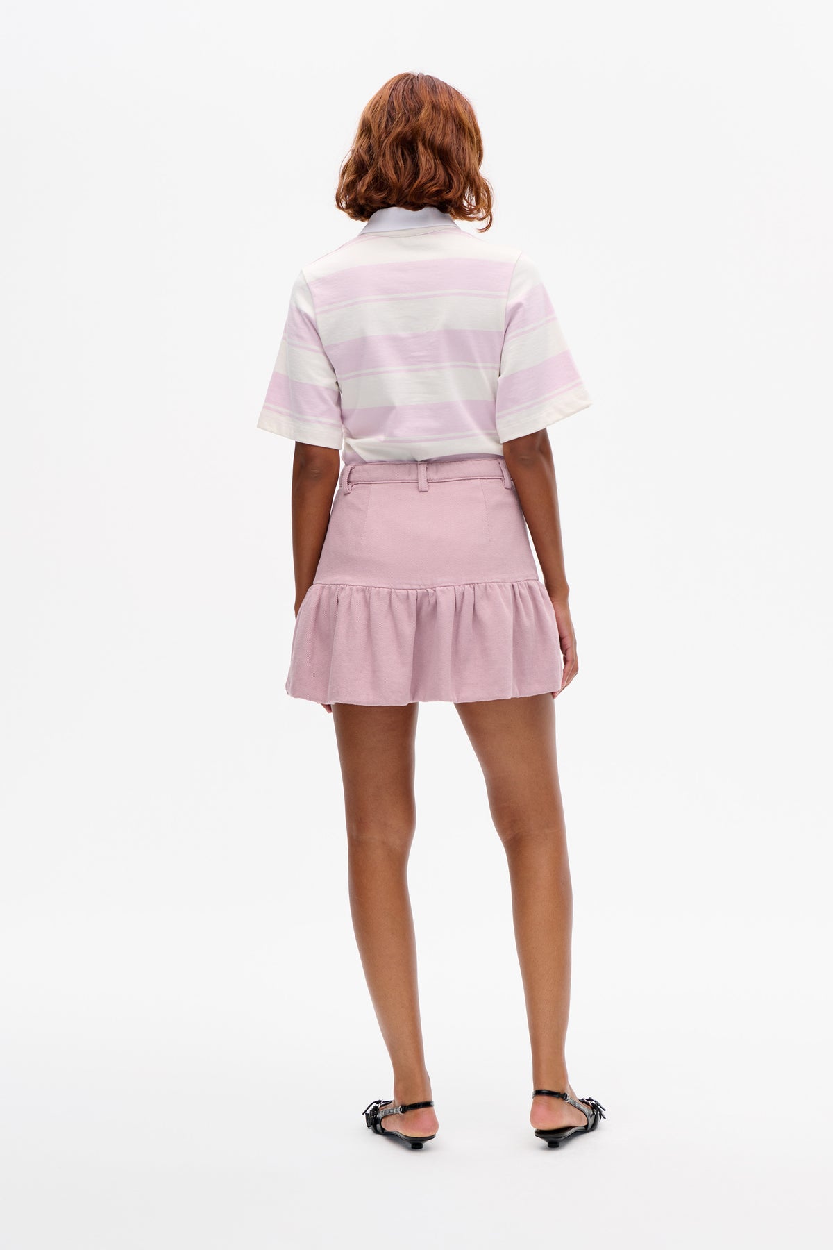 Back view of a model wearing a pale pink and cream striped short-sleeve polo shirt with a pink gathered mini skirt.