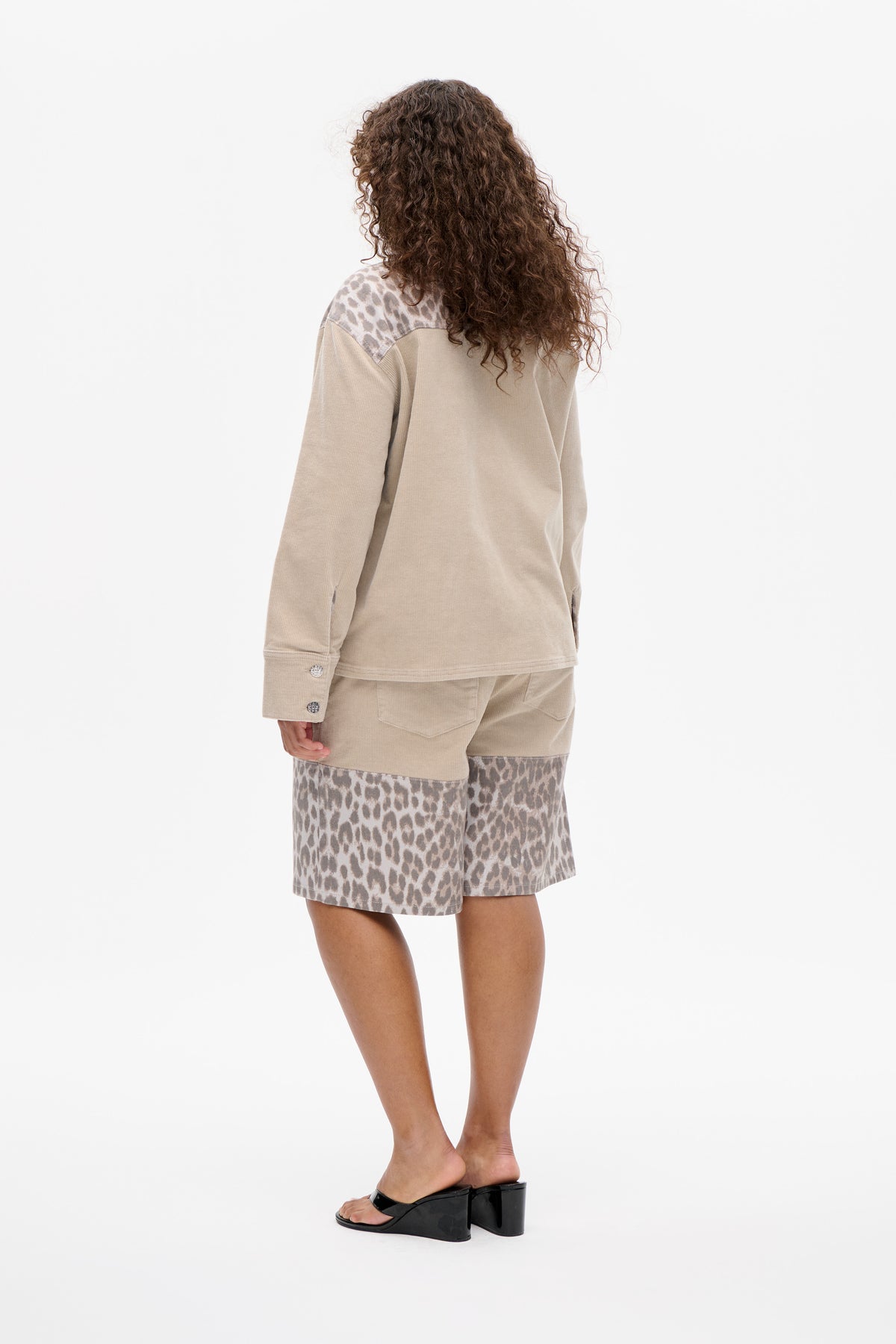 Back view of a model wearing a beige long-sleeved top with leopard-print shoulder panels and matching animal-print shorts.