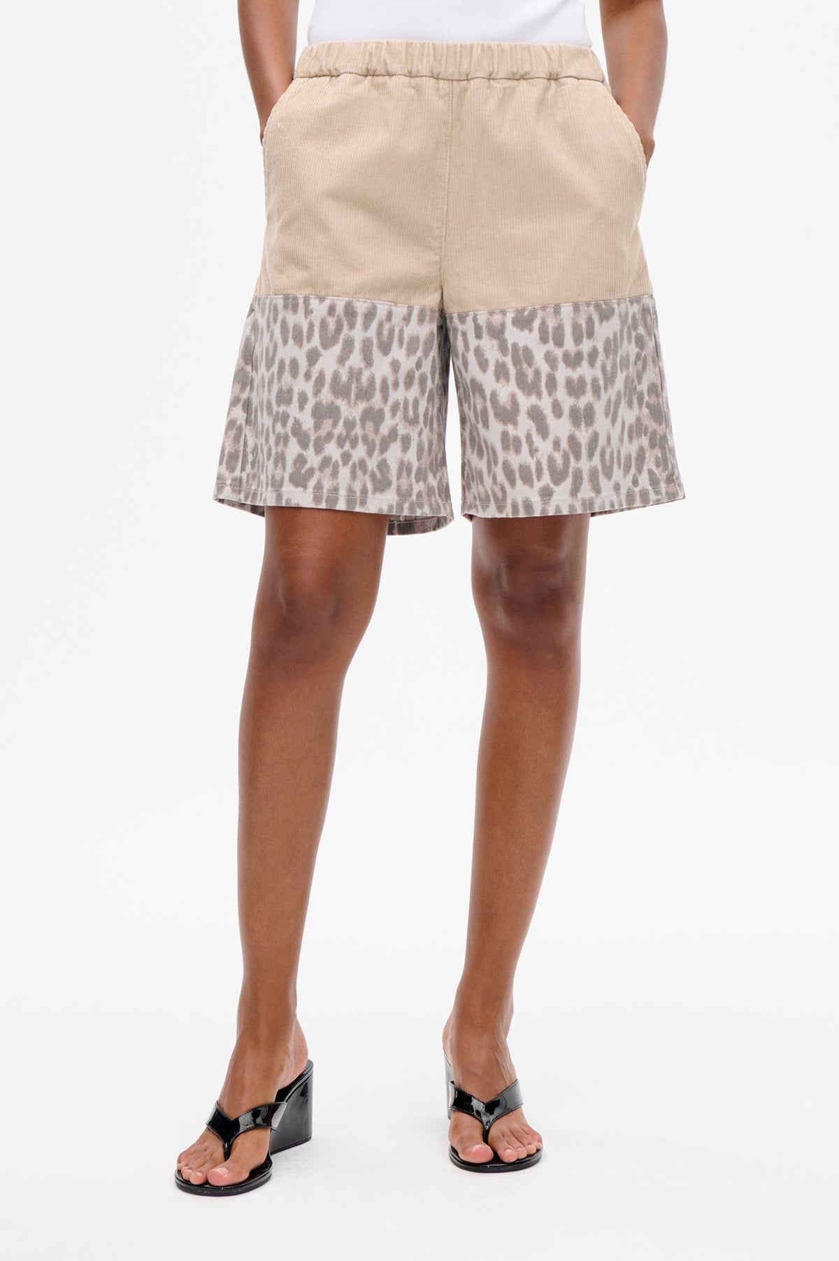 Front detail of shorts with a beige corduroy upper, elastic waistband and taupe leopard-print legs.