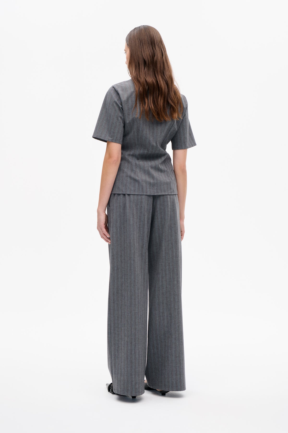 Back view of a model wearing a grey pinstripe short-sleeved top and matching wide-leg trousers.