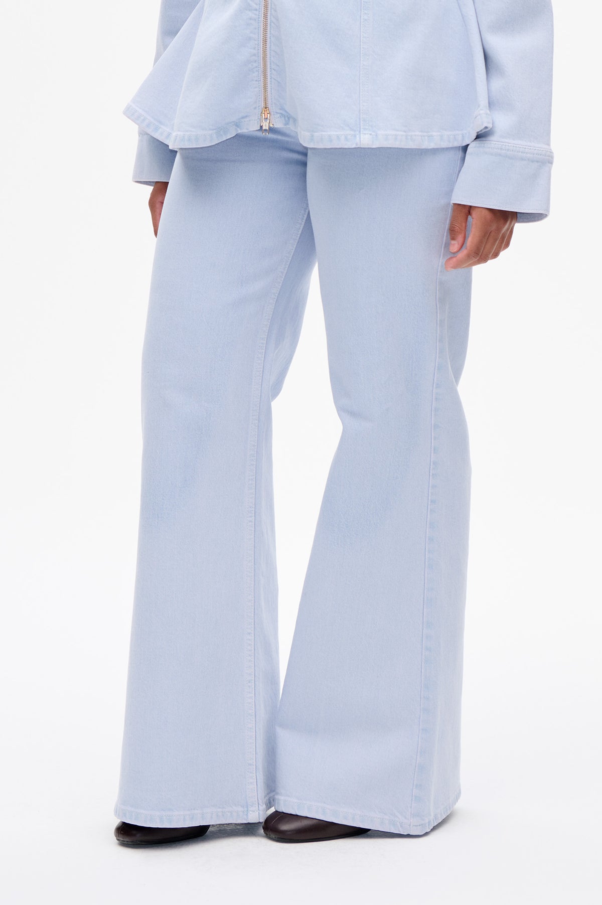 Close-up of a pale blue denim jacket with a metal zip, worn with wide-leg jeans.