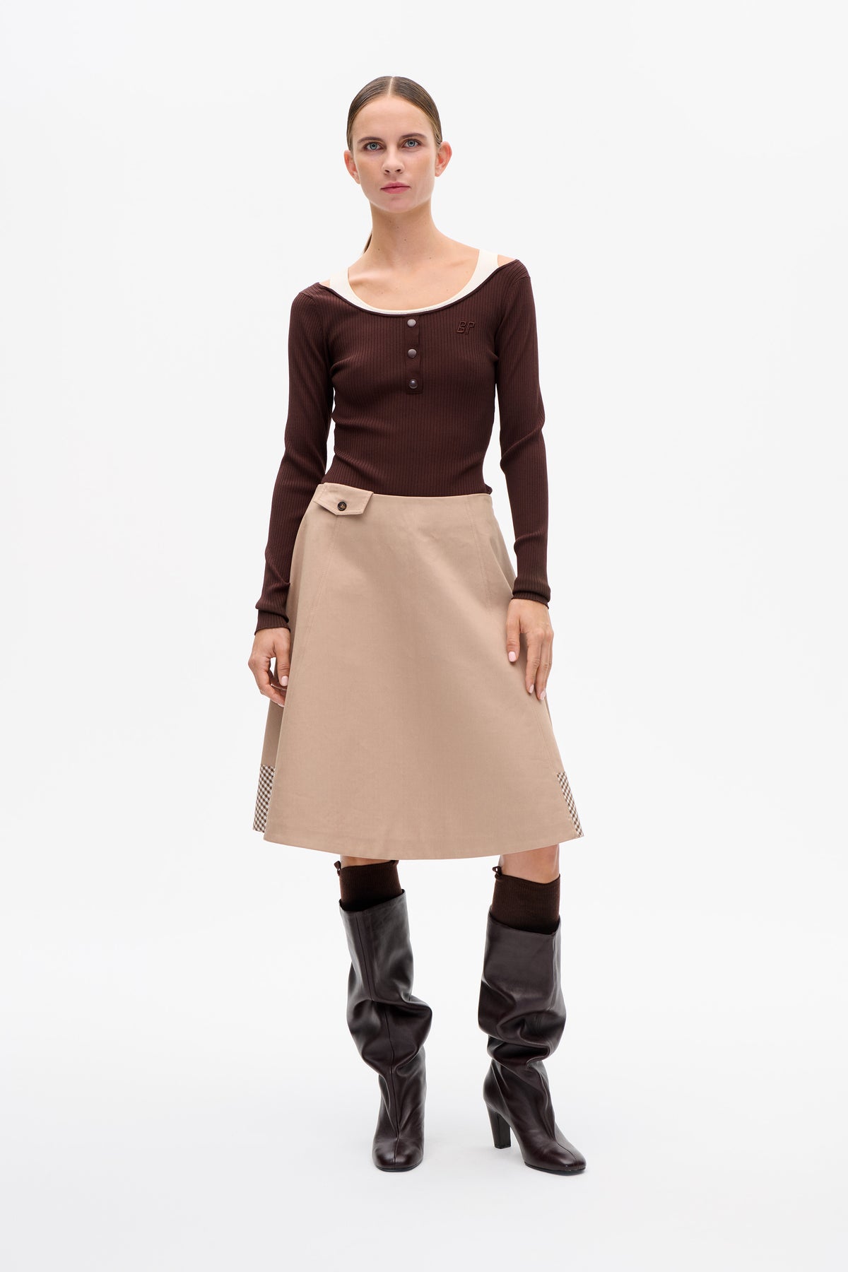 Model wearing a dark brown ribbed button-front top with a wide neckline and a beige A-line skirt with checked side panels.