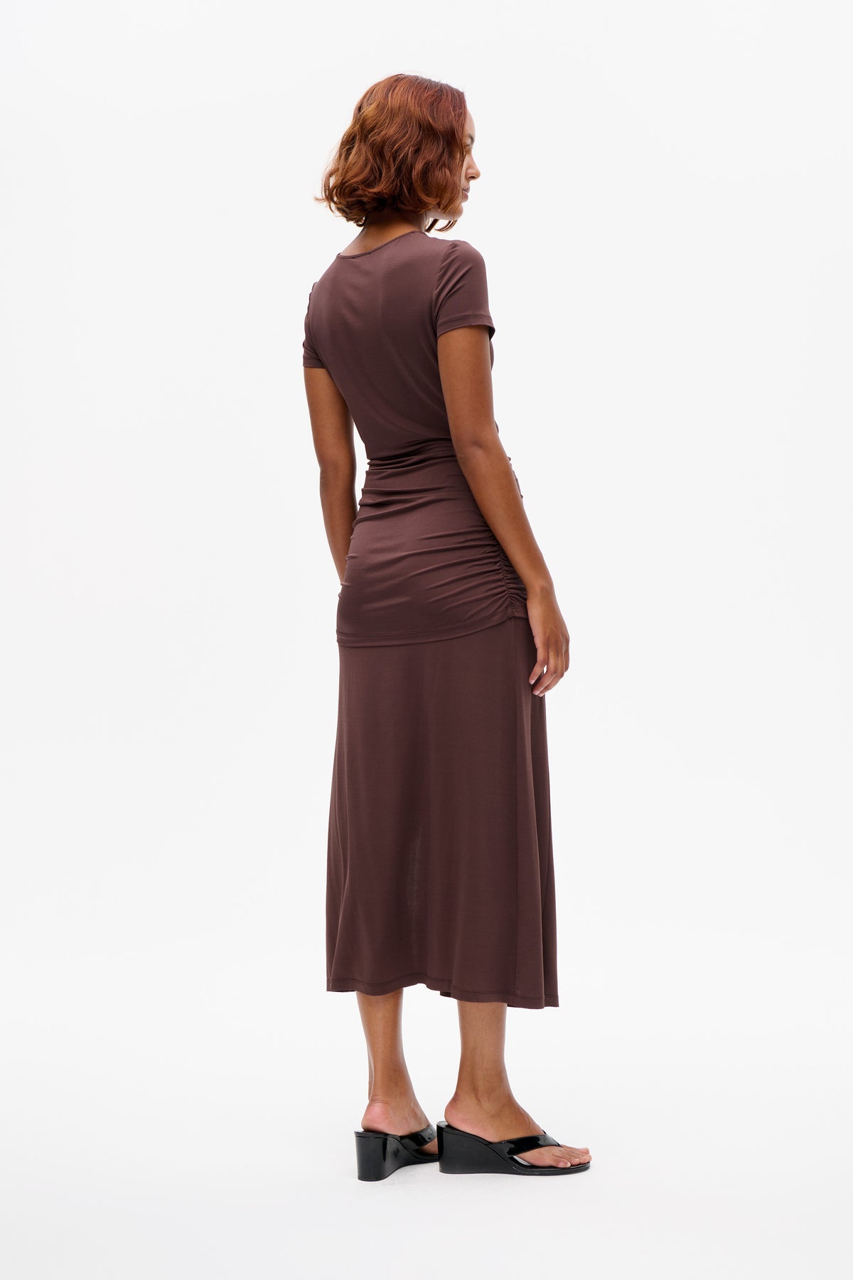 Model wearing a mauve short-sleeved midi dress with a ruched waist and side seam, shown from the back and side.