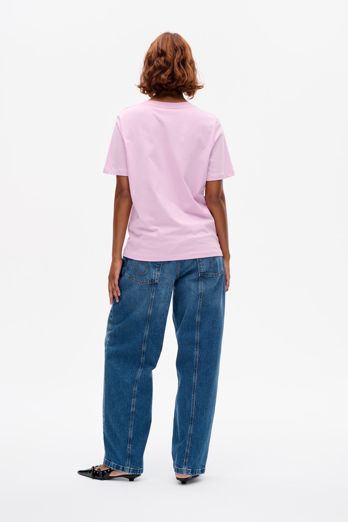 Back view of a model wearing a plain light pink short-sleeved T-shirt with blue wide-leg jeans.