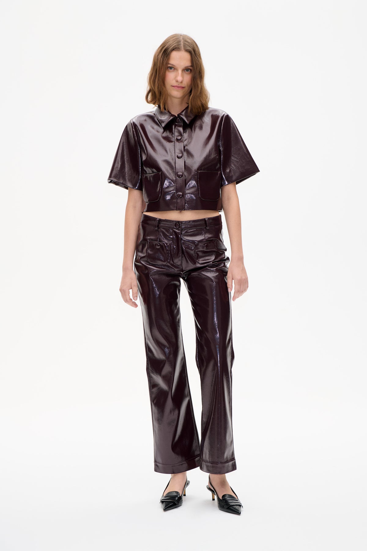 Front view of a model wearing a glossy dark plum short-sleeved button-front shirt with patch pockets and matching wide-leg trousers.