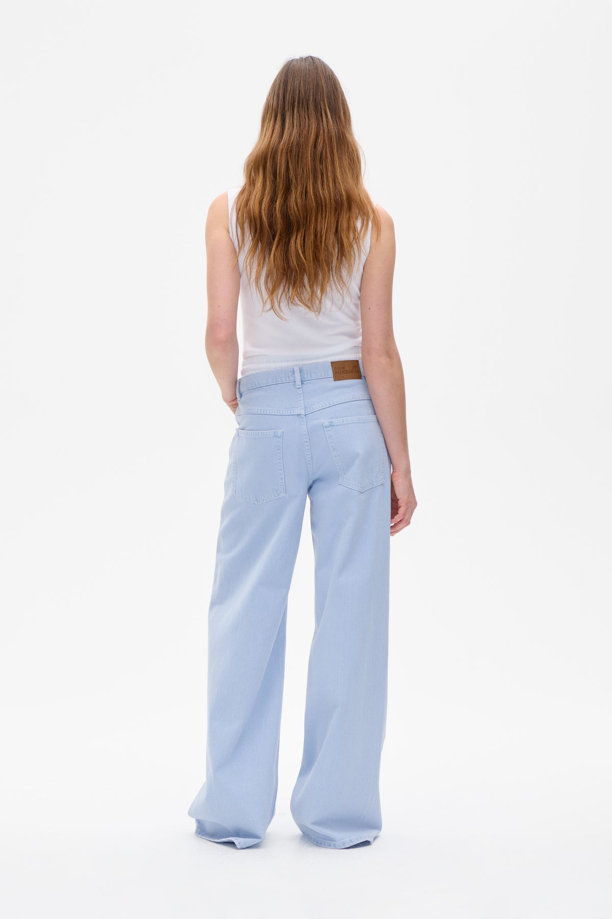 Back view of a model wearing pale blue wide-leg jeans with patch pockets and a white sleeveless top.