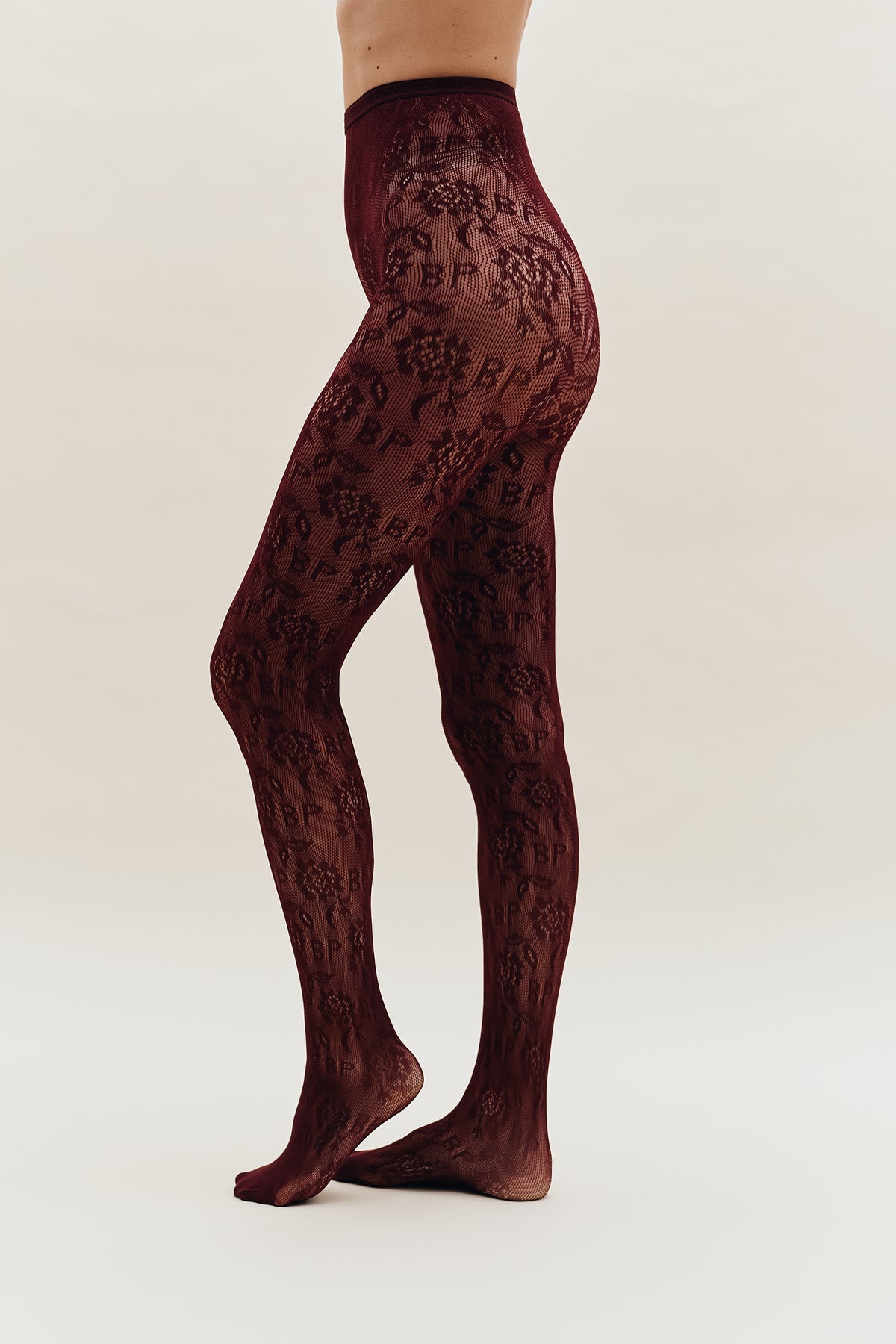Model wearing sheer burgundy tights with an all-over dark floral pattern, shown from waist to feet.